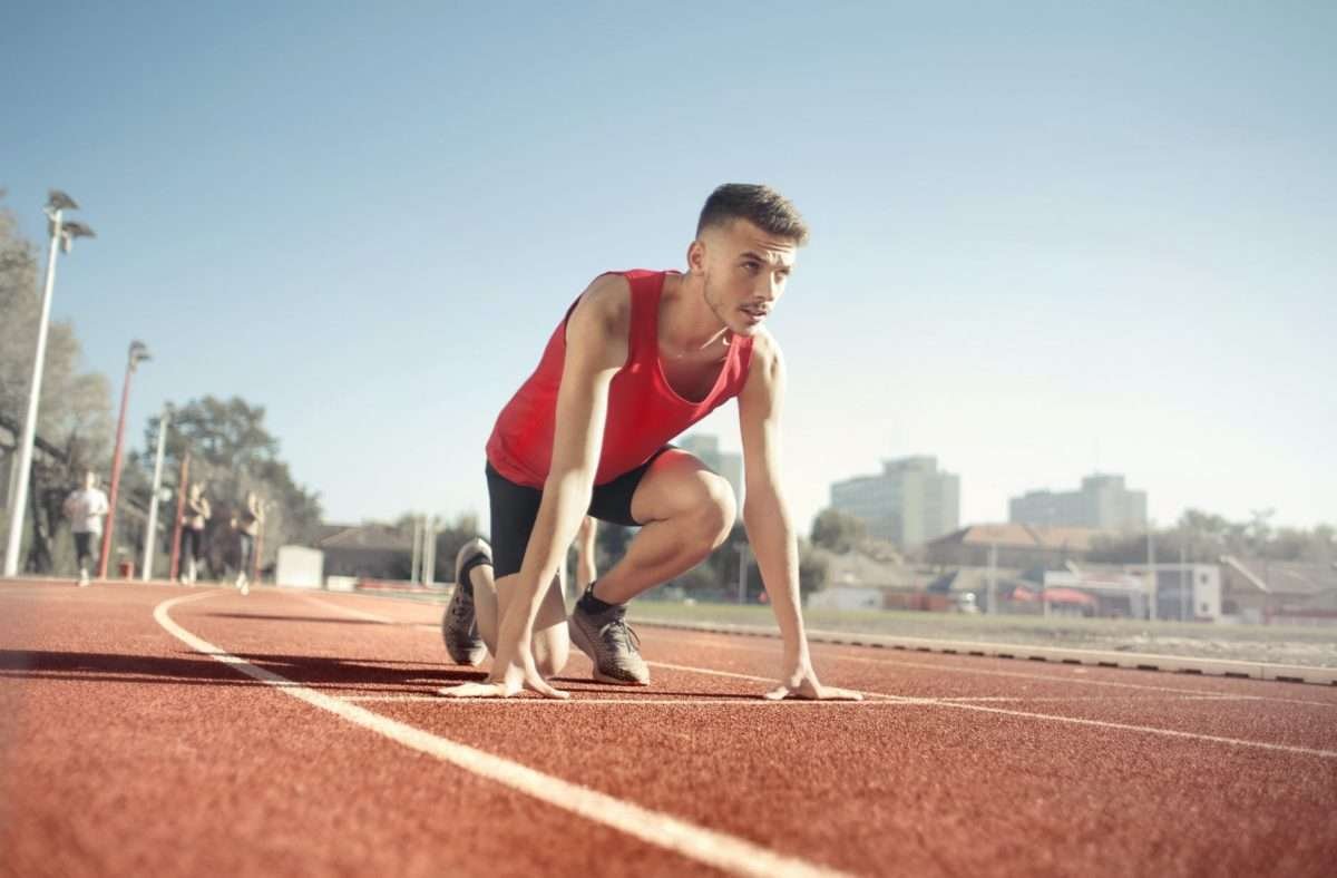 man in res tank top running on athletic field